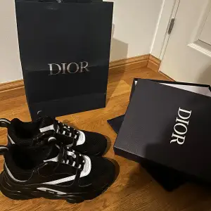 Säljer ett par snygga svarta sneakers från Dior i nytt skick. De har en stilren design med vita detaljer och snörning. Perfekta för både vardag och fest! Kommer i originalförpackning med tillhörande påse.