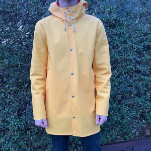 Signerad Stutterheim regnjacka  - Säljer en snygg gul cool Stutterheim regnjacka i strl M i mycket bra skick. Modellen på bilden är 185cm och den är lite liten. Den har långa ärmar och stängs med knappar framtill. Jackan har en hög krage med snörning för extra skydd mot regn. Perfekt för höst och vår när vädret är lite ostadigt. Passar både till vardags och när du är ute på äventyr! Galet modern jacka signerad av grundaren Alexander Stutterheim själv. Stor original papperspåse och tags medkommer.