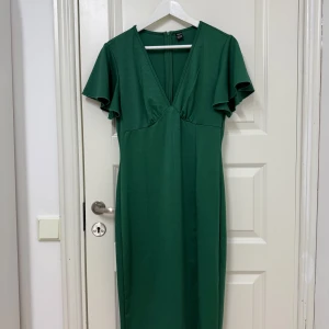 Grön klänning från Shein - Snygg grön klänning från Shein i storlek M. Den har en v-ringad design med kortärmade volanger och en dragkedja i ryggen. Perfekt för julen och nyåret som närmar sig! Helt ny, oanvänd och redo för en ny ägare som kommer rocka den!