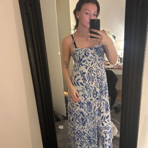 Vit och blå långklänning - Säljer en superfin vit och blå långklänning med ett snyggt blommigt mönster. Perfekt för sommardagar eller en avslappnad fest. Den har en luftig passform och är gjord i ett lätt material som känns skönt mot huden, knyts i ryggen🩷