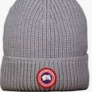 Grå stickad mössa från Canada Goose - Säljer en snygg och varm grå stickad mössa från Canada Goose. Den har en klassisk ribbad design och ett coolt märke framtill. Perfekt för kalla dagar! PRIS KAN DISKUTERAS.