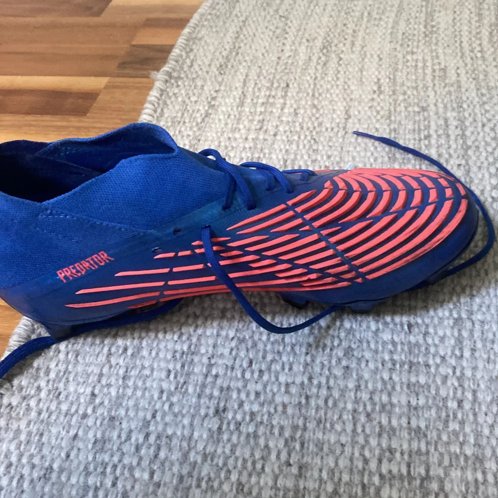 Säljer ett par Adidas Predator fotbollsskor i en cool blå och orange färgkombination. Skorna har en snygg design med snörning och är perfekta för fotbollsträning eller match. De är i bra skick och redo för nya äventyr på planen! Nypris 2300kr. Skor.