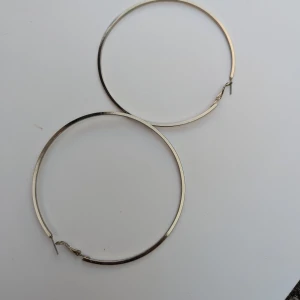 Stora silverfärgade hoop-örhängen - Säljer ett par stora och stilrena silverfärgade hoop-örhängen. De är perfekta för att ge en extra touch till vilken outfit som helst. Örhängena är i bra skick och har en enkel låsmekanism som gör dem lätta att ta på och av.Det är svårt att fånga den exakta färgen, men den är ljusguld.