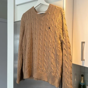 Beige stickad tröja från Polo Ralph Lauren - Säljer en snygg beige stickad tröja från Polo Ralph Lauren. Den har ett klassiskt flätmönster och den ikoniska loggan broderad på bröstet. Tröjan är långärmad och perfekt för både höst och vinter. Nypris: 2395kr! Skriv om ni har några frågor!