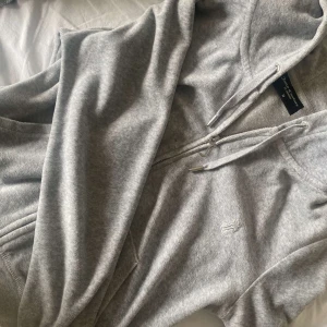 Grå hoodie från juicy caoture - Säljer en supermjuk och bekväm grå kofta från juicy couture. Den har en dragkedja framtill och en klassisk huva med dragsko. Perfekt för en avslappnad stil eller mysiga dagar hemma. Den har också praktiska fickor på sidorna.