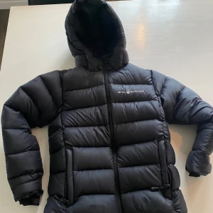 Svart dunjacka från Sail Racing säljes i storlek 140 - Säljer en svart dunjacka från Sail Racing i storlek 140✨ Superfint material och kvalitet. Perfekt för kalla vinterdagar. Några tecken på användning finns tex en minde lagning, se bild. Men fortfarande i bra skick✨ Passar både till vardags och utomhusaktiviteter. Nypris 2699:- säljes för 500:-