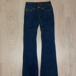 Mörkblå jeans från Gina Jeans - Snygga mörkblå jeans från Gina Jeans med bootcut-stil. De har dekorativa stjärndetaljer och knappar i bronsfärg. Perfekta för en avslappnad look.