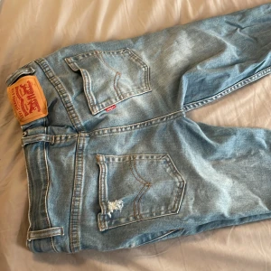 Levis jeans i ljusblå denim - Säljer ett par klassiska Levis jeans i ljusblå denim. De har en straight passform och är midwaist. Jeansen har slitningar på benen för en trendig look och en ikonisk Levis-lapp på baksidan.