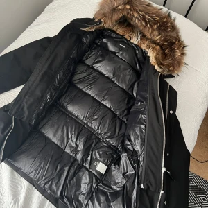 Mackage Edward - Säljer en snygg svart parkajacka från Mackage Edward i mycket bra skick. Jackan har en mysig pälsfodrad huva och är perfekt för kalla vinterdagar. Den har dragkedja och knappar framtill för extra skydd mot kylan. Använt max 2-3 gånger. Säljer pga för liten i storlek. 