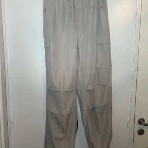 Beige cargobyxor från Shein - Säljer ett par beige cargobyxor från Shein med elastisk midja och dragsko. Byxorna har flera praktiska fickor och en loose passform, perfekt för en avslappnad stil.