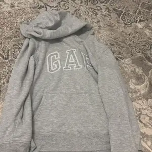 Säljer en klassisk grå hoodie från GAP med stor logga på bröstet. Tröjan har en bekväm passform med känguruficka och huva. Perfekt för en avslappnad stil.