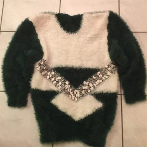 Tröja i mohair  - Säljer en supermysig och fluffig tröja i grönt och vitt med ett coolt mönster över bröstet. Perfekt för kalla dagar när du vill vara både varm och stilren. Tröjan har långa ärmar och en unik design som verkligen sticker ut. Passar perfekt för höst och vinter!