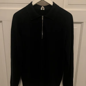 Svart half zip tröja från arket - Säljer en stilren svart tröja med dragkedja framtill. Den är tillverkad av 60% bomull, 30% linne och 10% ull, vilket gör den både bekväm och hållbar. Perfekt för både vardag och lite finare tillfällen. Passar bra till höst och vår.