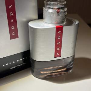 Säljer en elegant Prada Luna Rossa Eau de Toilette. Flaskan har en stilren design i silver och glas med en röd detalj och Pradas logotyp. Perfekt för den som söker en sofistikerad doft. Det är en 100ml flaska med ungefär 55ml kvar. Kan gå ner i pris vid snabb affär.