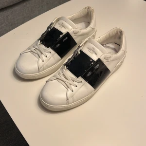 Valentino sneakers  - Snygga vita Valentino sneakers med en iögonfallande svart detalj över snörningen. Skorna har en klassisk design med rund tå och är tillverkade i skinn. Perfekta för en stilren look.