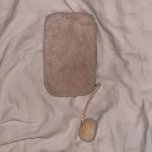 Babyrosa pälsig necessär  - Säljer en söt babyrosa plånbok med pälsig yta och dragkedja. Den har en fluffig boll som detalj på dragkedjan.
