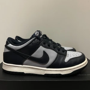 Nike Dunk i svart och grått - Snygga Nike Dunk sneakers i svart och grått med klassisk design. Skorna har snörning och en bekväm passform, perfekt för vardagsbruk.