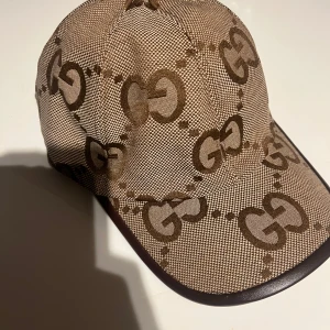 Beige jumbo gucci keps 🧢  - Snygg beige gucci keps med det ikoniska GG-mönstret. Kepsen har en justerbar rem baktill för perfekt passform. Perfekt accessoar för en stilren look.