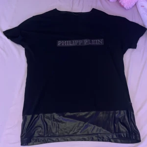 Svart t-shirt från Philipp Plein - Snygg svart t-shirt från Philipp Plein med korta ärmar och en glansig detalj längst ner. Perfekt för en stilren look med en touch av lyx.
