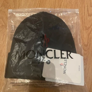 Svart ribbad mössa från Moncler - Snygg svart ribbad mössa från Moncler med logotyp framtill. Perfekt för kyliga dagar och ger en stilren look. Pris kan diskuteras👌🏽