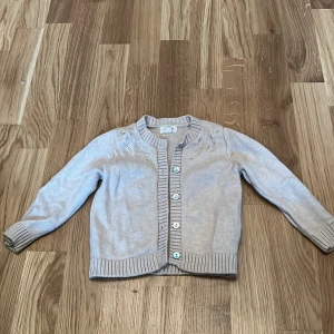 Beige kofta från Noa Noa Miniature - Söt beige kofta från Noa Noa Miniature med knappar framtill. Perfekt för de små under kyligare dagar. Koftan har ribbade kanter och är tillverkad i ett mjukt material.