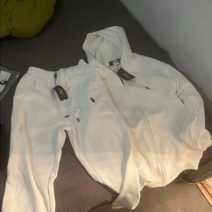 Vit hoodie och byxor från Polo Ralph Lauren - Säljer en snygg vit hoodie och matchande byxor från Polo Ralph Lauren. Hoodien har dragkedja och byxorna har en bekväm resår i midjan. Perfekt för en avslappnad stil eller mysiga dagar hemma. Båda plaggen är i nytt skick och redo att användas! Köpt är köpt tar ej tbx 