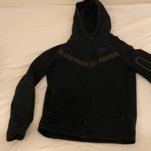 Svart hoodie från Nike storlek  - Säljer en svart hoodie från Nike med dragkedja och huva. Jackan har långa ärmar och en stilren design med diskreta detaljer. Perfekt för en avslappnad stil.