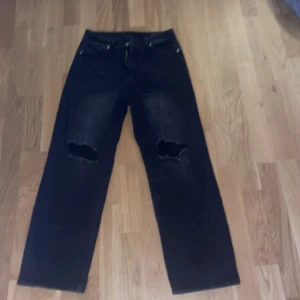 Svarta jeans med slitningar - Säljer ett par svarta jeans i bra skick med coola slitningar på knäna. De har dragkedja och knapp. Perfekta för en avslappnad stil!