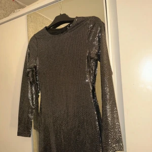 Glittrig klänning med öppen rygg - Snygg glittrig klänning i silver med långärmad design och en elegant öppen rygg. Perfekt för en kväll ute eller en festlig tillställning. Klänningen har en tight passform som framhäver figuren.