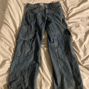 Weekday Cargojeans - Säljer ett par blå cargobyxor från Weekday. Byxorna har flera praktiska fickor och en avslappnad passform. Perfekta för en casual look.