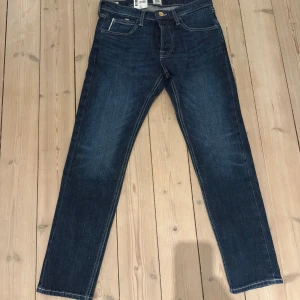 Mörkblå jeans från Lee - Säljer ett par snygga mörkblå jeans från Lee i modellen Luke Button Fly. De har en slim tapered passform. Jeansen är i nytt skick och har en klassisk design.