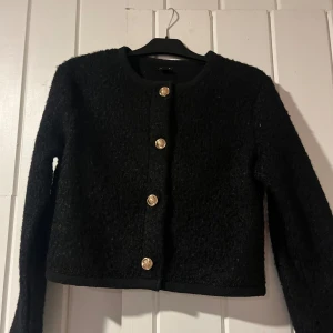 Svart kofta guldknappar - Svart kofta i mycket bra skick med guldknappar framtill. Den har en klassisk och elegant stil, perfekt för både vardag och fest. Materialet känns mjukt och bekvämt, oanvänd