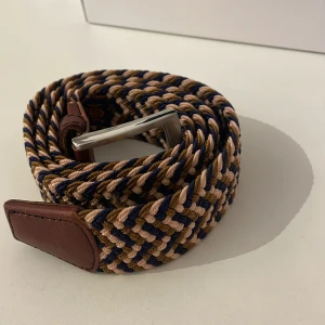 Flätat bälte  - Säljer ett snyggt flätat bälte i beige och blått med bruna läderdetaljer. Bältet har hög kvalitet och är i skick 9,5/10, knappt använt. Det passar till många olika stilar för många olika tillfällen. Passar till alla storlekar av midjor då det har hål överallt. Tveka inte på att höra av er vid frågor eller liknande så svarar jag så snabbt jag kan!☺️🙌🤝