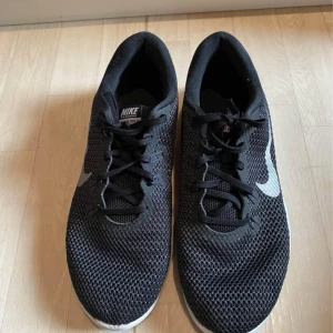Svarta Nike sneakers - Säljer ett par svarta Nike sneakers i bra skick. De har en stilren design med vit sula och klassisk Nike-logga på sidan. Skorna är i syntetmaterial och har snörning för bra passform. Perfekta för både träning och vardag! Pris kan diskuteras!!