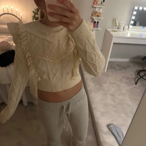 Stickad tröja med volangdetaljer - Säljer en superfin krämvit stickad tröja med volangdetaljer. Den är croppad och har ett snyggt mönster. Perfekt för höst och vår! Tröjan har långa ärmar och är i mycket bra skick. Passar perfekt till både vardag och fest.