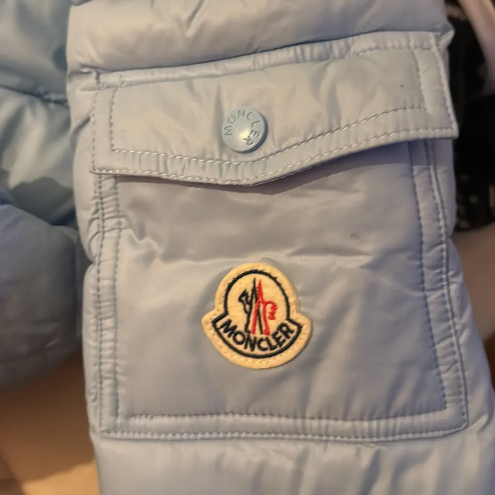 Säljer en snygg ljusblå dunjacka med märket Moncler jackan har en huva och dragkedja. Jackan har ett broderat Moncler-märke på ärmen och en unik serietidningsetikett på insidan. Perfekt för kyliga dagar! Och perfekt för dig som har stil. Ställ fler frågor privat!!. Jackor.