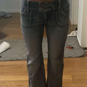 Blå bootcut jeans - Snygga blå bootcut jeans med låg midja och dubbla knappar fram. Perfekta för en avslappnad stil med en touch av retro. De har en klassisk femficksdesign och en lätt tvättad look.