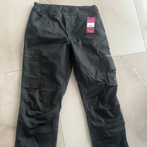 Svarta jobbyxor från Bluewear - Säljer två par svarta jobbbyxor från Bluewear i storlek 38 och 40. Byxorna har flera praktiska fickor med dragkedja och knappstängning. Perfekta för en avslappnad och funktionell stil. Båda är oanvända 