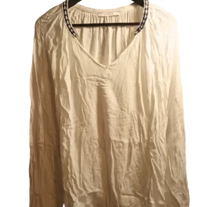 Vit blus från Joelle - Säljer en luftig vit blus från Joelle med dekorativa svarta detaljer vid hals och ärmslut. Blusen har en v-ringad design och långa ärmar med knappdetalj. Perfekt för en stilren look.