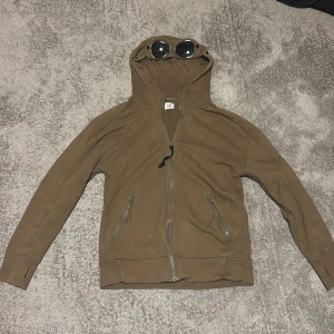 Cp company hoodie - Säljer en cool olive grön hoodie från C.P. Company i storlek S. Den har en unik design med glasögon i huvan och dragkedja framtill. Perfekt för höst och vår, och ger en riktigt snygg streetwear-look. Materialet är mjukt och bekvämt, perfekt för vardagsbruk. Köpt på thernlunds i Nacka forum pris diskuteras vid snabb affär