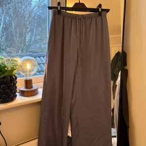 Grå byxor från H&M - Säljer ett par grå byxor från H&M i storlek S. De har en loose passform med elastisk midja och snörning för extra komfort. Perfekta för en avslappnad stil eller hemmamys. Materialet känns mjukt. En liten fläck se bild 2