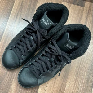 Svarta sneakers från Puma - Säljer ett par svarta Puma sneakers i mycket bra skick. De har en snygg och stilren design med snörning och en mjuk, fluffig insida för extra komfort. Perfekta för höst och vinter med sitt varma foder. Sulan är i bra skick och ger bra grepp. Passar både till vardags och lite mer avslappnade tillfällen. Använt fåtal ggr som nya