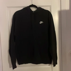 Svart hoodie från Nike - Säljer en klassisk svart hoodie från Nike i storlek S. Den är superbekväm och perfekt för både träning och chill. Hoodien har en vit Nike-logga på bröstet och en praktisk känguruficka framtill. Perfekt för höst och vinter!