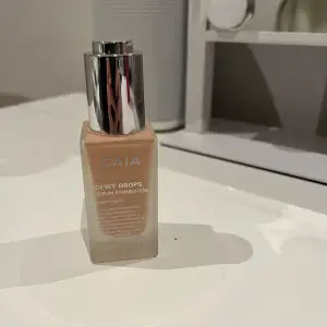 Säljer en CAIA Dewy Drops Serum Foundation i en snygg glasflaska med silverlock. Den har en lätt och fuktgivande formula som ger en naturlig lyster. Perfekt för en fräsch och glowig look! Flaskan innehåller 30 ml. Färg 20C, använd 2-3 gånger.