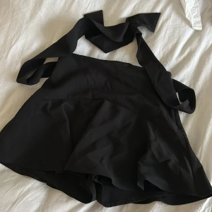 Svart kjol med knytband - Snygg svart kjol med volang och knytband i midjan. Perfekt för en stilren look. Kjolen har en kort längd och ger en elegant touch till din outfit. Storlek M