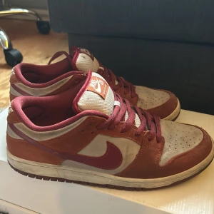 Nike Dunk SB ”Dark Russet” - Säljer ett par ett par Nike Dunk SB ”Dark Russet” i storlek 42.5. Köpta för ett par år sen och använda men inte skadade. Finns ett svart märke på skornas tunga men kanske går att rengöra. Nypris på Stockx är 4.6k säljer dessa för under 1399kr så vid rengöring kan man få en profit. Inget OG