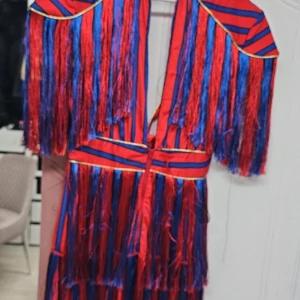 Röd och blå randig klänning med fransar - Unik klänning i rött och blått med randigt mönster och fransdetaljer. Klänningen har en djärv design med fransar som ger en extra touch. Perfekt för den som vill sticka ut.
