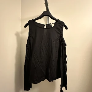 Svart topp med öppna axlar - Snygg svart topp med öppna axlar och långa ärmar. Perfekt för en kväll ute eller en fest. Den har en lös passform. Oanvänd från hm i storlek M!