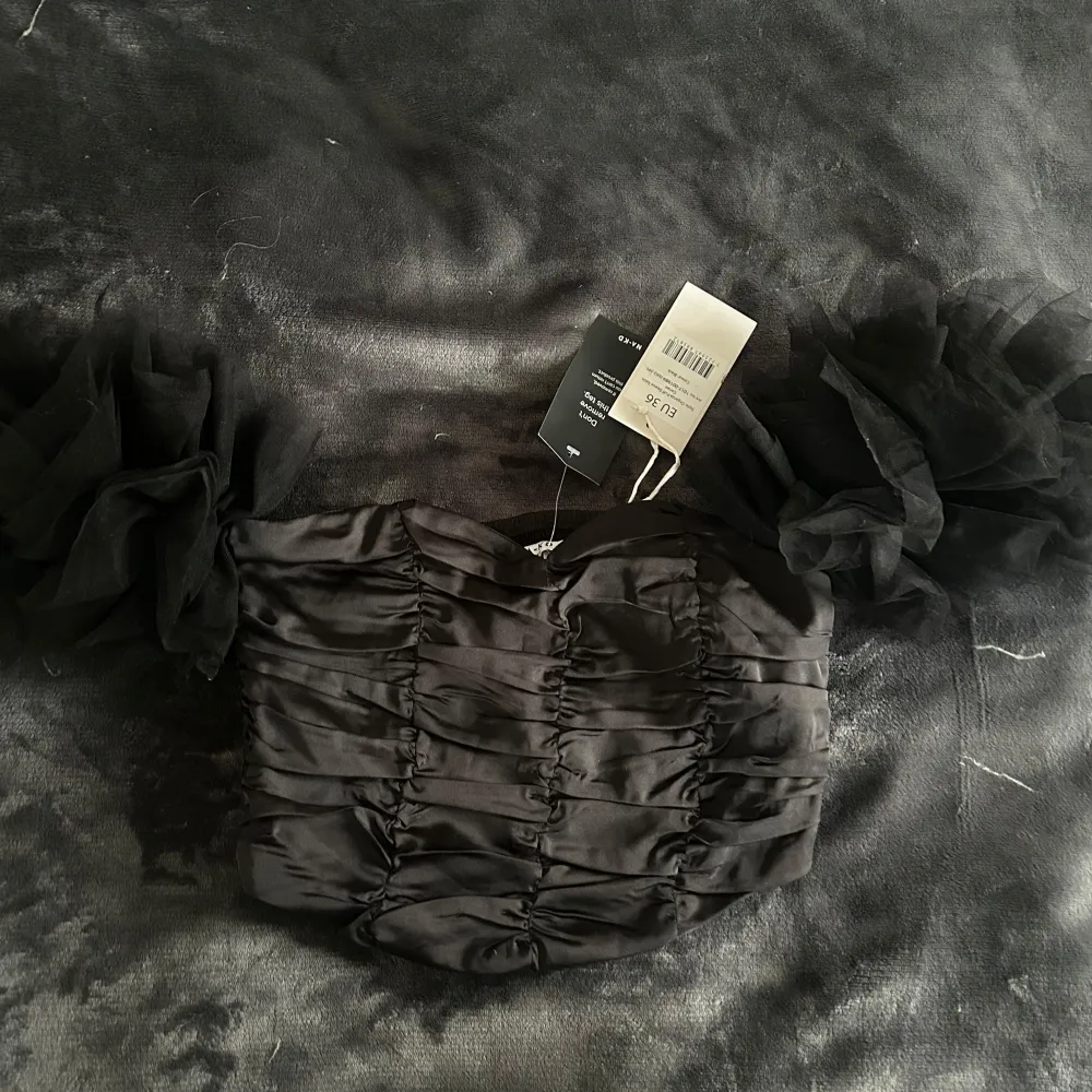 Snygg svart offshoulder topp från NA-KD med volangdetaljer på ärmarna. Toppen har en åtsittande passform med rynkade detaljer framtill. Perfekt för en kväll ute eller en speciell tillställning.. Yläosat.
