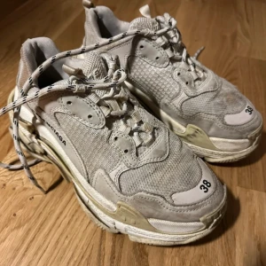 Balenciaga sneakers i beige - Säljer ett par Balenciaga sneakers i beige med snörning och robust sula. Skorna har en modern design med märkets logga på sidan och nummerdetalj framtill. Se bild för skav i hälen, går enkelt att laga.